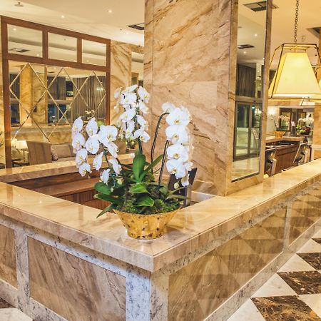 Windsor Marapendi Hotel Rio de Janeiro Zewnętrze zdjęcie The photo depicts a luxurious hotel lobby featuring a polished marble reception desk. There are elegant white orchids arranged in a gold pot on the counter, adding a touch of sophistication. The surrounding interior showcases marble walls, stylish li